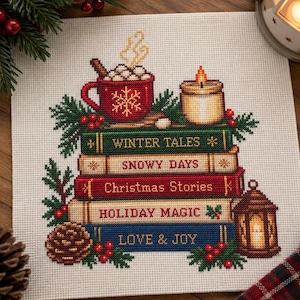 May include: A cross-stitch pattern on fabric featuring a stack of five books titled Winter Tales, Snowy Days, Christmas Stories, Holiday Magic, and Love & Joy. Above the books sits a red mug with a snowflake, a candle, and pine branches.