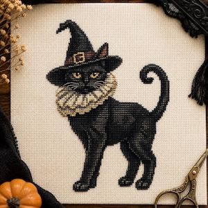 Könnte beinhalten: Eine Kreuzstichstickerei auf hellbeigem Stoff, die eine schwarze Katze mit einem spitzen schwarzen Hexenhut mit goldener Schnalle und einem gerüschten cremefarbenen Kragen zeigt. Die Katze hat gelbe Augen und einen geringelten Schwanz.