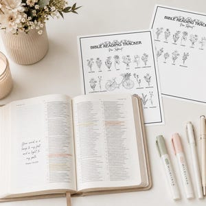 Op de afbeelding: Twee witte vellen papier met de titel Bible Reading Tracker New Testament met zwarte lijntekeningen van bloemen, een open Bijbel met gemarkeerde tekst, een brandende kaars in een glazen pot en vijf pennen in neutrale tinten op een vlak.