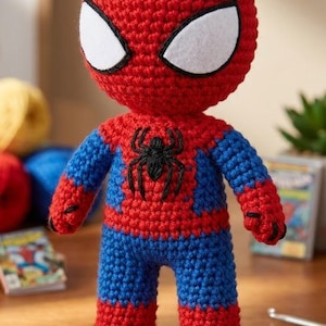 May include: A handmade crochet doll featuring the iconic red and blue color scheme of a superhero. The figure has a large, round head with white felt eyes outlined in black, and a black spider emblem embroidered on the center of the chest.