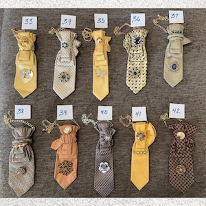 May include: A collection of ten decorative neckties numbered 33 through 42, each featuring unique fabric patterns, gold-tone chains, and various embellishments like brooches, buttons, and charms in yellow, brown, and grey color palettes.