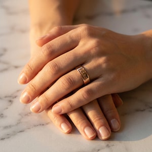 May include: A gold-toned band ring featuring the name Lisa engraved in a clear, sans-serif font. The ring has a smooth, polished finish and a flat profile, encircling the finger with a consistent width and a reflective metallic surface.