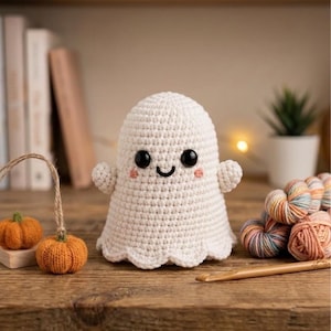 May include: A white crocheted ghost figurine with black plastic eyes, a stitched black mouth, and small pink embroidered cheeks. The ghost has a rounded head, two small arms, and a scalloped bottom edge, crafted with visible yarn stitches.