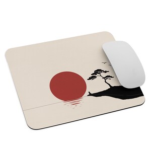 May include: A rectangular mouse pad with a cream-colored background featuring a graphic illustration of a large red sun, a black silhouette of a small tree on a landmass, and a white computer mouse resting on the right side of the surface.