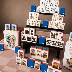 May include: A set of white mahjong tiles with blue backs, featuring various illustrations including lightning bolts, trees, treasure chests, and joker cards. Some tiles display the text CRAK, BAM, and JOKER, while others show Oklahoma-themed imagery.