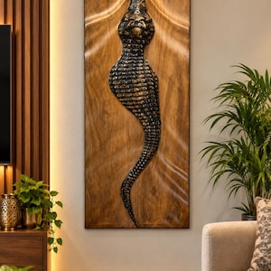 May include: A rectangular wooden wall art piece featuring a three-dimensional, dark-toned crocodile sculpture carved into the centre. The wood panel has a wavy, rippled surface texture, and the crocodile has a detailed, textured scale pattern.