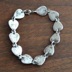 May include: A silver-toned chain bracelet composed of multiple flat, teardrop-shaped links with a distressed, textured finish. The bracelet features a secure lobster claw clasp mechanism that connects the ends of the circular link arrangement.