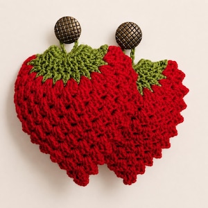 May include: Two strawberry-shaped crochet items made from red yarn with green yarn leaves at the top. Each piece features a round, metallic bronze-coloured button with a textured grid pattern attached to the top centre of the green leaves.