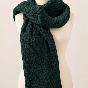 May include: A dark forest green knitted scarf with a textured, chunky stitch pattern. The scarf is wrapped around a mannequin neck, featuring a thick, dense weave that creates a consistent, uniform appearance throughout the entire length of the fabric.
