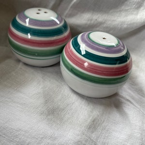 May include: Two spherical salt and pepper shakers with a white base and colorful horizontal stripes in shades of purple, teal, pink, and green. Each shaker has a small hole on top for dispensing the contents.