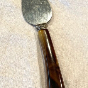 Può includere: Un server per torte vintage con una lama in acciaio inossidabile e un manico marmorizzato marrone e beige. Il server ha un design classico, adatto per servire torte, crostate e altri dessert. Il manico misura circa 13 cm.