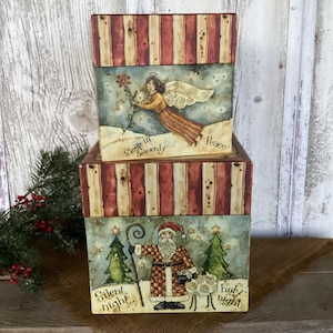 May include: Two stacked square decorative boxes with red and cream striped lids. The top box features an angel holding a flower with the text Sleep in heavenly Peace. The bottom box shows Santa Claus with a staff, trees, and a sheep with the text Silent night holy night.