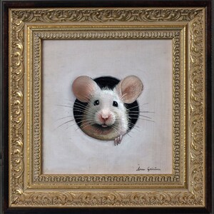 Puede incluir: Un rat&oacute;n blanco con orejas rosas asoma por un agujero en un lienzo blanco. El rat&oacute;n tiene la nariz negra y bigotes. El lienzo est&aacute; enmarcado en un marco dorado adornado.