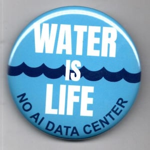 May include: A circular pinback button with a light blue background. It features a dark blue wave graphic and the white text WATER IS LIFE. Below the wave, the text NO AI DATA CENTER is printed in dark blue along the bottom edge of the button.
