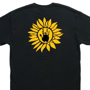 May include: Black t-shirt with a yellow sunflower graphic featuring a black handprint in the center.