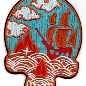 May include: An embroidered patch with a red and orange sailboat on a blue sea with white waves. The sailboat has white sails and is sailing under a white cloud in a blue sky. The patch is shaped like a skull with a red flame on the bottom.