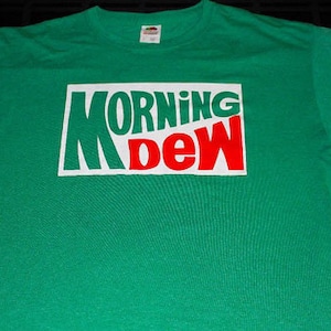 May include: Green t-shirt with a white box and the words "MORNING DEW" in white and red letters.