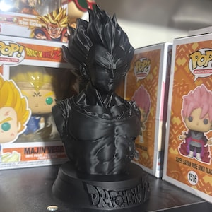 May include: A matte black 3D printed bust of the character Vegeta from Dragon Ball Z, featuring his signature spiky hair and muscular torso. The base of the bust is circular and displays the embossed Dragon Ball Z logo on the front.