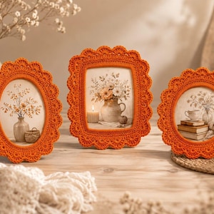 Può includere: Tre cornici per foto all'uncinetto di colore arancione vivace con bordi smerlati. Due cornici sono di forma ovale e una è rettangolare. Ogni cornice contiene un'immagine stampata di una natura morta con fiori, vasi, libri e una candela accesa.