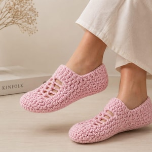Pode incluir: Um par de chinelos de crochê rosa claro com um padrão de malha texturizada e um design decorativo recortado na parte superior do pé. Os chinelos têm uma biqueira arredondada e uma abertura baixa, proporcionando um ajuste firme no tornozelo.