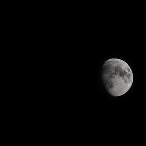 May include: A waxing gibbous moon set against a deep black night sky. The lunar surface displays visible craters, grey and white textures, and distinct shadows along the terminator line, capturing the celestial body in high contrast detail.