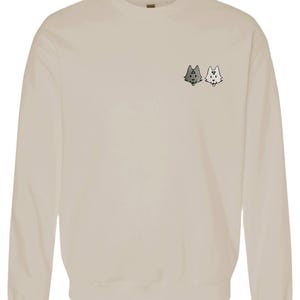 A beige sweatshirt with a small graphic design on the front, featuring two cartoon-like cat faces.