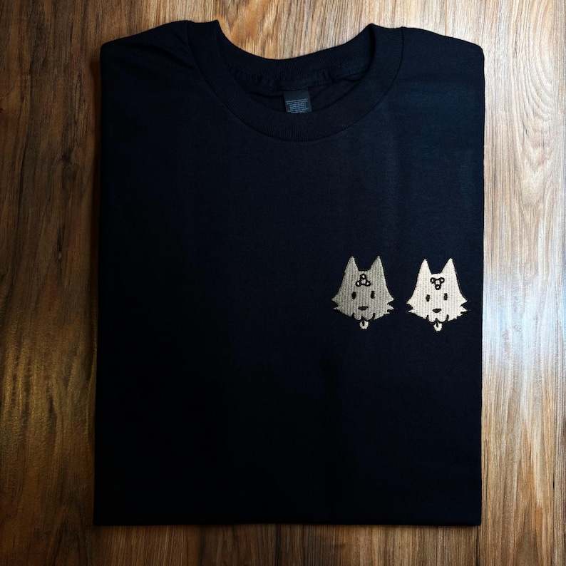 a black t-shirt with a small embroidered design of two cartoon dog faces on the front.