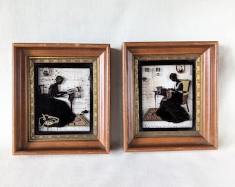 May include: Two framed silhouette art pieces in wooden frames. The frames are brown with gold accents. The art pieces are black silhouettes of women in vintage clothing. One piece shows a woman sitting and sewing, the other shows a woman sitting and reading.