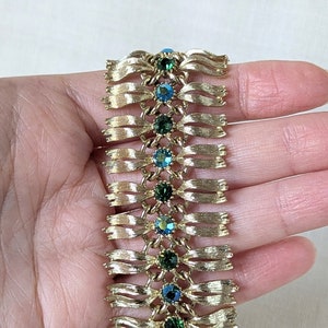 May include: A gold tone bracelet with a chain link design and green and blue rhinestones.