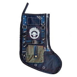 May include: Black and green Christmas stocking with a skull and flames design. The stocking has a zipper on the side and a small pocket on the front.
