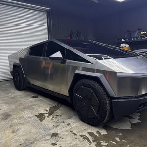 Puede incluir: Una camioneta eléctrica de acero inoxidable con un diseño de carrocería afilado, angular y en forma de cuña. El vehículo presenta un exterior plateado metálico, tapacubos negros, ventanas tintadas oscuras y una barra de luz frontal.