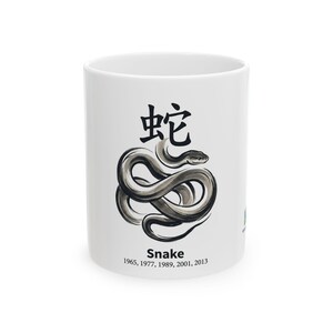 Könnte beinhalten: Ein weißer Keramikbecher mit einer schwarzen Tuschezeichnung einer zusammengerollten Schlange. Über der Schlange steht das chinesische Schriftzeichen für Schlange. Unter der Abbildung steht der Text "Snake" sowie die Jahre 1965, 1977, 1989, 2001, 2013.