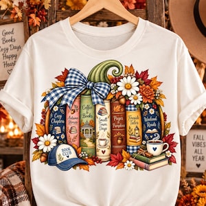 May include: A cream-colored t-shirt featuring a graphic of a pumpkin made of stacked books with titles like Cozy Chapters, Autumn Stories, Coffee & Books, Small Town Days, Pages & Pumpkins, Fireside Tales, and Weekend Reads, accented with a blue plaid bow.
