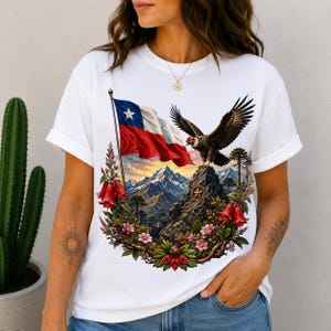 Könnte beinhalten: Ein weißes Kurzarm-T-Shirt mit einem Grafikdruck der chilenischen Flagge, die über einer Berglandschaft weht, mit einem fliegenden Andenkondor, umgeben von einem Kranz aus roten glockenförmigen Blüten und rosa Blumen auf einem Felsgipfel.