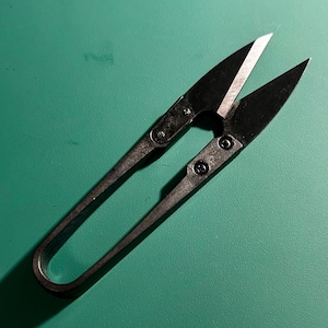 May include: Black sewing shears with a silver blade on a green surface.