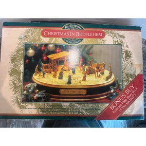 以下が含まれることがあります： Mr. Christmas Christmas In Bethlehem Collectiblesのアニメーション付きキリスト降誕セットが入った長方形の段ボール箱。箱には、フィギュア、厩舎、ラクダが描かれた円形のキリスト降誕シーンのグラフィックと、Christmas In Bethlehemという文字が印刷されています。