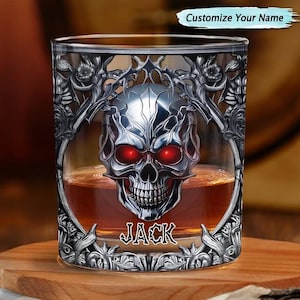 Puede incluir: Un vaso transparente lleno de líquido ámbar, con un gráfico de calavera plateada metálica con ojos rojos brillantes y detalles de filigrana. El nombre JACK está impreso en una fuente gótica debajo de la calavera. El texto dice Customize Your Name.