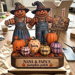 Könnte beinhalten: Eine Tischdekoration mit zwei Vogelscheuchen mit Kürbisköpfen, die Latzhosen und Hüte tragen. Ein Holzschild trägt die Aufschrift 'Tis the season' und 'NANA & PAPA'S pumpkin patch'. Vier kleine Kürbisse sind mit den Namen Quin, Randy, Eddy und Yvonne beschriftet.