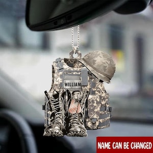 May include: A hanging car ornament featuring a camouflage tactical vest with the name WILLIAM printed on a rectangular patch, a matching camouflage helmet, and a pair of combat boots with a small American flag dog tag hanging between them.