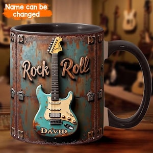 Puede incluir: Una taza de cerámica con asa e interior negros, con un gráfico de una guitarra eléctrica color verde azulado sobre un fondo de metal oxidado. El texto "Rock Roll" aparece en letra cursiva y el nombre "DAVID" está impreso en el cuerpo de la guitarra.