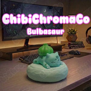 May include: A light green Bulbasaur figurine resting on a circular, textured light green base. The character features a prominent green bulb on its back and closed eyes. The text "ChibiChromaCo Bulbasaur" is overlaid in white with a pink outline.