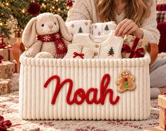 Könnte beinhalten: Ein cremefarbener, gerippter Aufbewahrungskorb mit braunen Ledergriffen und dem Namen Noah in roter Schreibschrift. Darin befinden sich ein Plüschhase mit rotem Schal, eine cremefarbene Strickjacke und ein Lebkuchenmann-Aufnäher auf der Vorderseite.