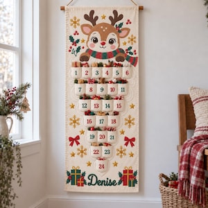 Peut inclure: Un calendrier de l'Avent en tissu vertical orné d'un renne de dessin animé portant une écharpe. Il comporte vingt-quatre poches numérotées disposées en forme de sapin, décorées de flocons, de nœuds et du prénom Denise inscrit en bas.
