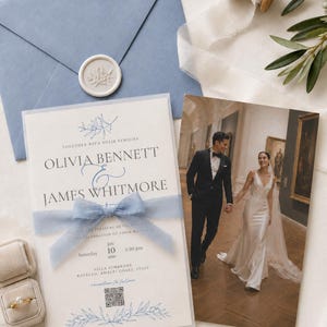 May include: A wedding invitation suite featuring a blue envelope with a white wax seal, a translucent vellum overlay tied with a blue ribbon, and a photograph of a couple. The text includes the names Olivia Bennett and James Whitmore.