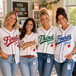 May include: Four white baseball-style jerseys with thin vertical pinstripes, each featuring a different grade level text in script: First Grade in red, Second Grade in orange, Third Grade in green, and Fourth Grade in blue, with a small red apple icon.