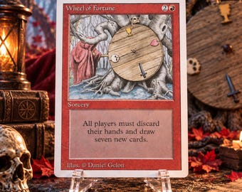May include: A Magic: The Gathering trading card titled Wheel of Fortune with a red border. The illustration depicts a wooden wheel mounted on a tree with a figure in a red cloak. The text reads: All players must discard their hands and draw seven new cards.