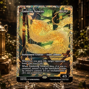 May include: A rectangular trading card titled Enduring Tenacity featuring a shimmering, golden, translucent snake illustration. The card has a holographic foil finish, black text boxes, and displays the creature type Enchantment Creature - Snake Glimmer with a power and toughness of 4/3. The card includes game rules text and set information at the bottom.