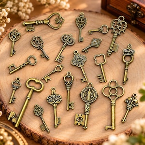 May include: A collection of twenty-one antique-style brass-toned metal key charms in various shapes and sizes. Each key features intricate decorative bows, shafts, and bits, designed as pendants or craft embellishments with small loops.