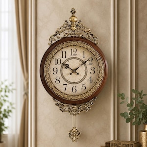 May include: A wall clock with a dark brown circular frame and an off-white face featuring black Arabic numerals. The clock is adorned with ornate gold-toned metal filigree at the top and bottom, including a decorative pendulum hanging below.