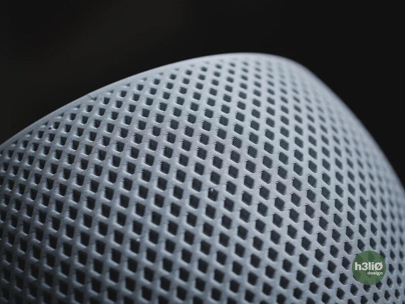 Puede incluir: Un objeto esf&eacute;rico de color gris claro que presenta un patr&oacute;n de rejilla en forma de diamante que se repite en su superficie curva. Un peque&ntilde;o logotipo circular verde con el texto blanco h3li&oslash; design es visible en la esquina inferior derecha.